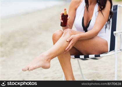 summer, travel, body care and people concept - close up of young woman in swimsuit sunbathing on folding chair and spraying sunscreen oil to her skin