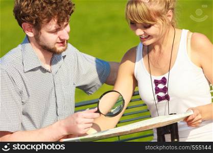 Summer travel concept. Young tourist couple on vacation in city looking up directions on map holding magnifying glass . Tourist couple in city looking up directions on map