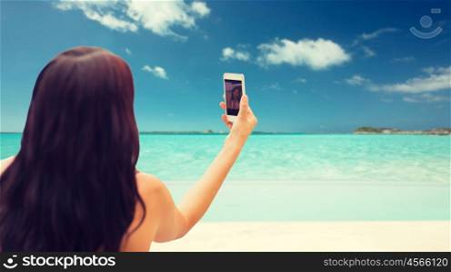 summer, travel, technology and people concept - close up of sexy young woman taking selfie with smartphone over tropical beach background