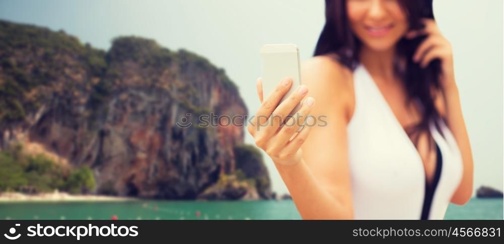 summer, travel, technology and people concept - close up of sexy young woman taking selfie with smartphone over bali beach and rock background