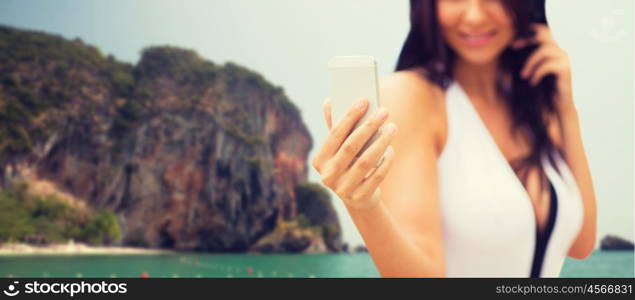 summer, travel, technology and people concept - close up of sexy young woman taking selfie with smartphone over bali beach and rock background