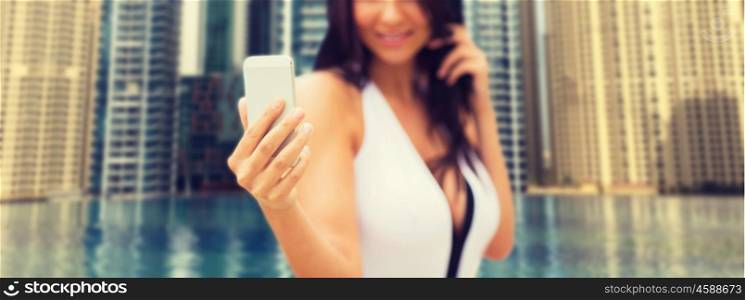 summer, travel, technology and people concept - close up of sexy young woman taking selfie with smartphone over infinity edge pool in dubai city background