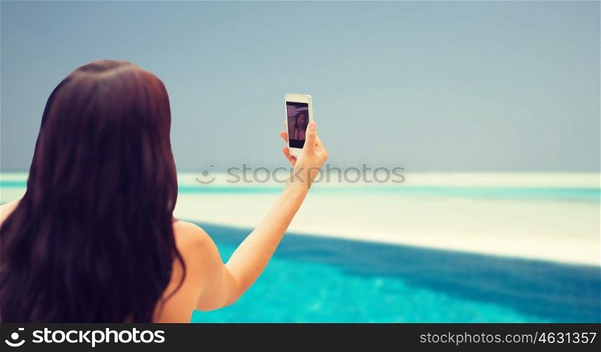 summer, travel, technology and people concept - close up of sexy young woman taking selfie with smartphone over beach and swimming pool background. young woman taking selfie with smartphone
