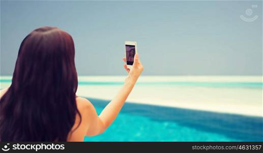 summer, travel, technology and people concept - close up of sexy young woman taking selfie with smartphone over beach and swimming pool background. young woman taking selfie with smartphone