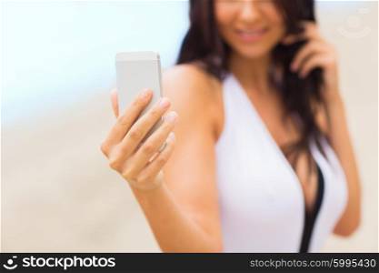 summer, travel, technology and people concept - close up of sexy young woman taking selfie with smartphone on beach