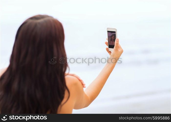 summer, travel, technology and people concept - close up of sexy young woman taking selfie with smartphone on beach