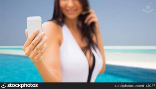 summer, travel, technology and people concept - close up of sexy young woman taking selfie with smartphone over beach and swimming pool background