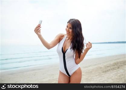 summer, travel, technology and people concept - sexy young woman taking selfie with smartphone on beach
