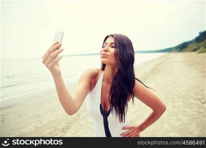 summer, travel, technology and people concept - sexy young woman with smartphone taking selfie of duck face on beach