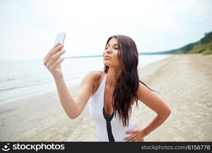 summer, travel, technology and people concept - sexy young woman with smartphone taking selfie of duck face on beach