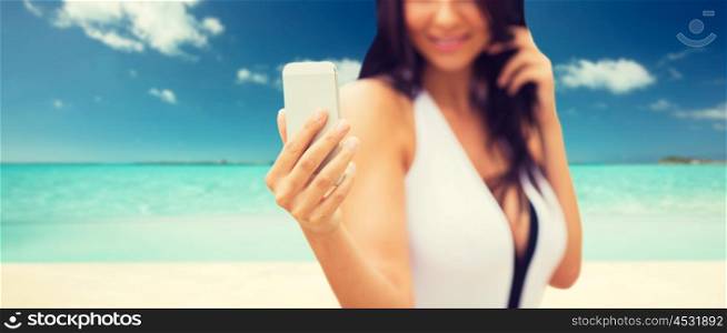 summer, travel, tourism, technology and people concept - close up of sexy young woman taking selfie with smartphone over tropical beach background