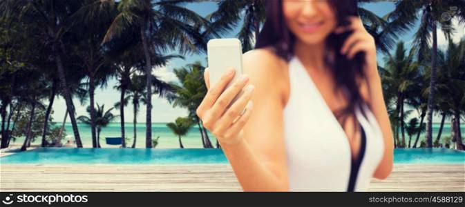 summer, travel, tourism, technology and people concept - close up of sexy young woman taking selfie with smartphone over resort beach with palms and swimming pool background