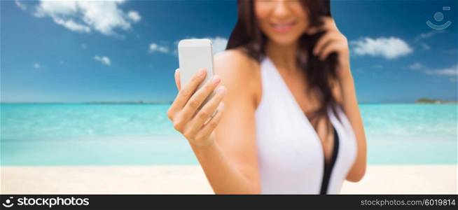 summer, travel, tourism, technology and people concept - close up of sexy young woman taking selfie with smartphone over tropical beach background