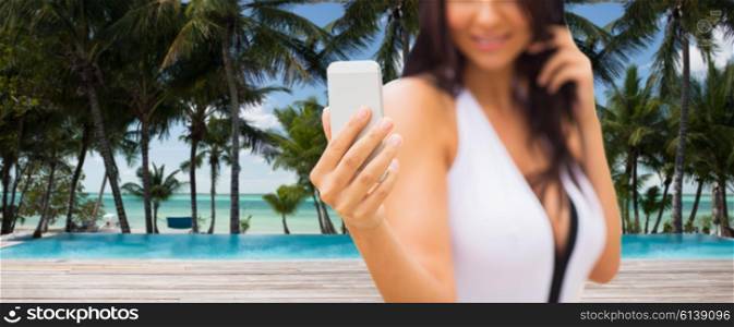 summer, travel, tourism, technology and people concept - close up of sexy young woman taking selfie with smartphone over resort beach with palms and swimming pool background
