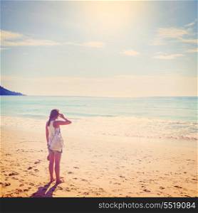 summer travel. young woman is standing on beach with aeroplane flying above