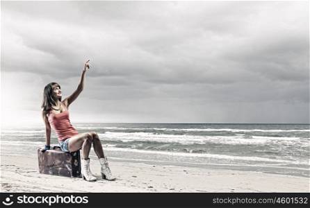 Summer traveling. Young woman tourist sitting on suitcase at seaside