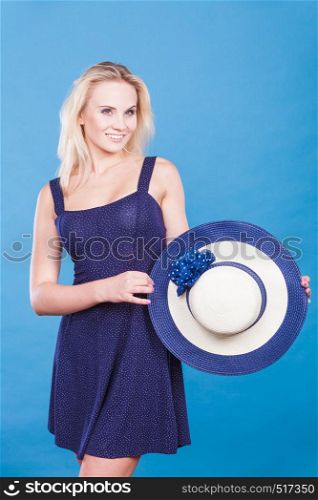 Summer trendy fashionable outfit ideas concept. Blonde attractive woman wearing short blue cocktail dress holding sun hat. Woman wearing short navy dress holding sun hat