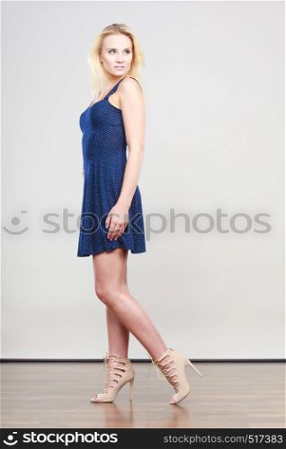 Summer trendy fashionable outfit ideas concept. Blonde attractive woman wearing short blue cocktail dress and fancy high heels.. Blonde woman wearing short navy cocktail dress