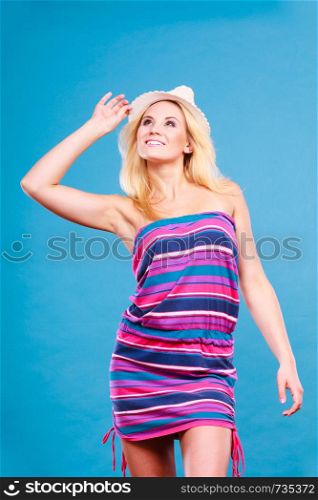 Summer trendy fashionable outfit ideas concept. Blonde woman wearing short colorful striped strapless dress and white sun hat. Blonde woman wearing short colorful striped dress