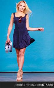 Summer trendy fashionable outfit ideas concept. Woman wearing short navy dress holding flip flops and sunglasses.. Woman wearing short dress holding flip flops and sunglasses