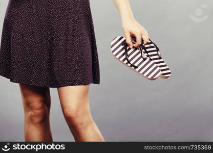 Summer trendy fashionable outfit ideas concept. Woman wearing short navy dress holding flip flops. Woman wearing short navy dress holding flip flops