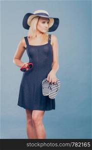 Summer trendy fashionable outfit ideas concept. Woman wearing short navy dress sun hat holding flip flops and sunglasses.. Woman wearing short dress holding flip flops and sunglasses