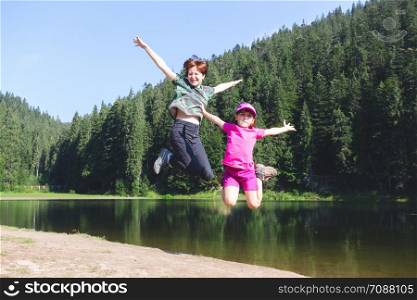Summer - two sisters on a hike. Fun happy family jumping on the shore of a mountain lake synevyr.
