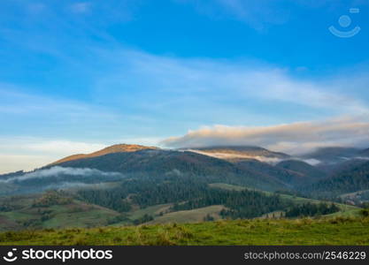 Summer Ukrainian Carpathians and sunny morning. Light mist between wooded mountains. The first rays of the sun illuminate the mountain peaks. Sunrise Fog over the Wooded Ukrainian Carpathians