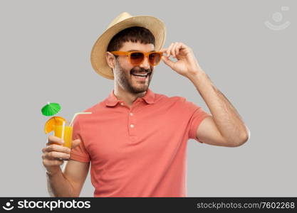 summer, vacation and people concept - happy smiling young man in sunglasses and straw hat with orange juice cocktail over grey background. happy man in straw hat with orange juice cocktail