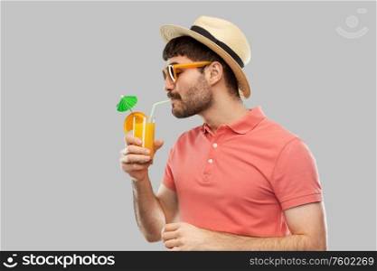 summer, vacation and people concept - happy smiling young man in sunglasses and straw hat drinking orange juice cocktail over grey background. man in straw hat drinking orange juice cocktail
