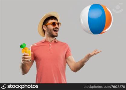 summer, vacation and people concept - happy smiling young man in sunglasses and straw hat with orange juice cocktail and inflatable beach ball over grey background. happy man with orange juice and beach ball
