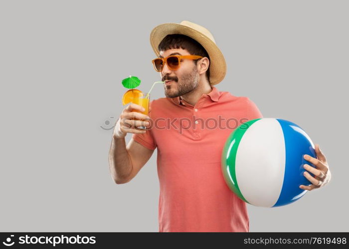 summer, vacation and people concept - happy smiling young man in sunglasses and straw hat with orange juice cocktail and inflatable beach ball over grey background. happy man with orange juice and beach ball