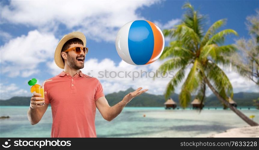 summer, vacation and people concept - happy smiling young man in sunglasses and straw hat with orange juice cocktail and inflatable beach ball over tropical beach background in french polynesia. happy man with orange juice and beach ball