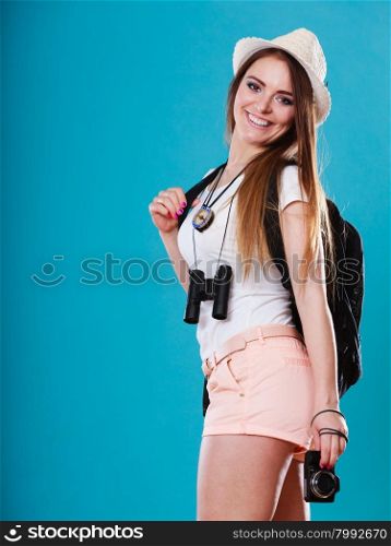 Summer vacation and tourism concept. Smiling woman in straw hat with backpack binocular camera in hand on blue