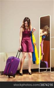 Summer vacation and travel concept. Woman preparing packing to trip, standing with clothes and bag suitcase at home