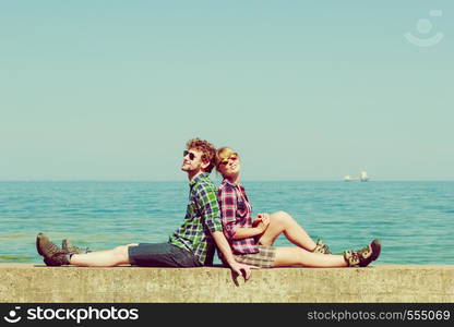 Summer vacation and traveling concept. Young hiking couple woman man relaxing after hike on sea shore enjoying sunlight