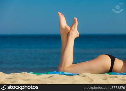 Summer vacation. Closeup of female legs. Sexy girl sunbathing tanning on the beach. Young woman relaxing on the sea coast. Summertime.