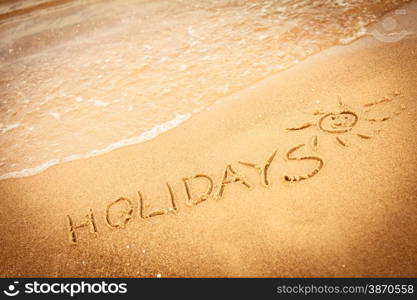 Summer vacation concept. The word holidays written in the sand on beach.