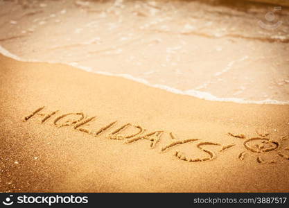 Summer vacation concept. The word holidays written in the sand on beach.