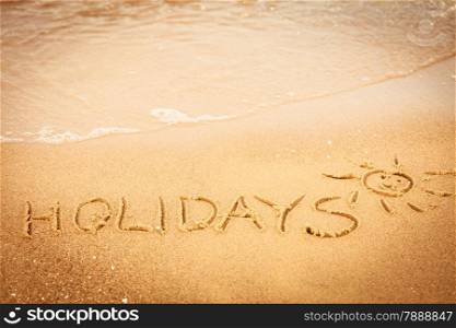 Summer vacation concept. The word holidays written in the sand on beach.