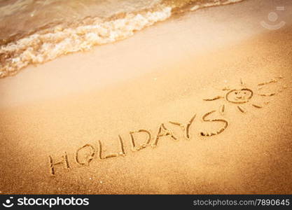 Summer vacation concept. The word holidays written in the sand on beach.