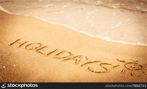 Summer vacation concept. The word holidays written in the sand on beach.