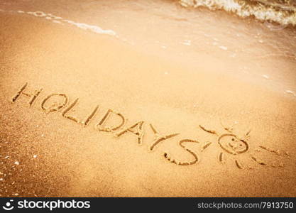 Summer vacation concept. The word holidays written in the sand on beach.