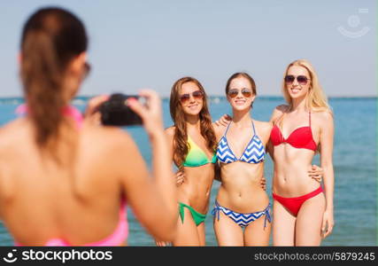 summer vacation, gesture, travel and people concept - group of smiling young women photographing by camera and waving hands on beach