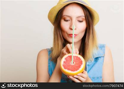 Summer vacation. Happy funny girl tourist in hat holding grapefruit citrus drinking juice from fruit on gray.