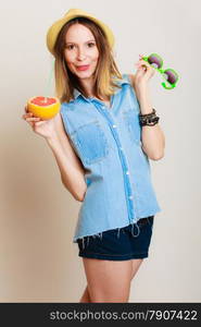 Summer vacation. Happy funny girl tourist in sunglasses and hat holding grapefruit citrus drinking juice from fruit on gray.