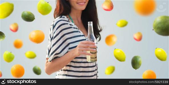 summer vacation, holidays, drinks and people concept - close up of smiling young woman drinking from bottle over fruits and berries on gray background