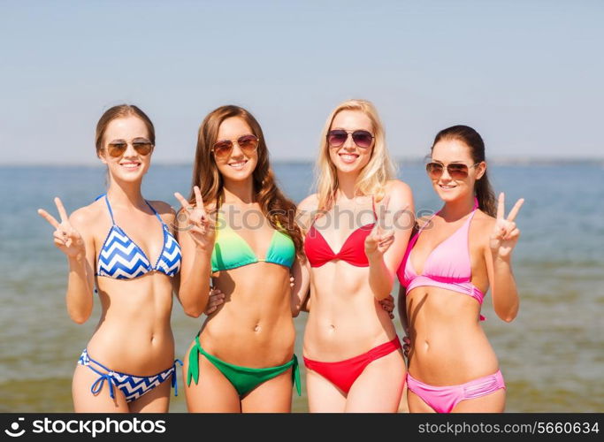 summer vacation, holidays, gesture, travel and people concept- group of smiling young women showing peace or victory sign on beach