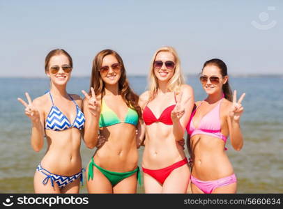 summer vacation, holidays, gesture, travel and people concept- group of smiling young women showing peace or victory sign on beach