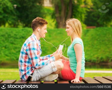 summer, vacation, holidays, technology and friendship concept - smiling couple with smartphone and earphones sitting on bench in park